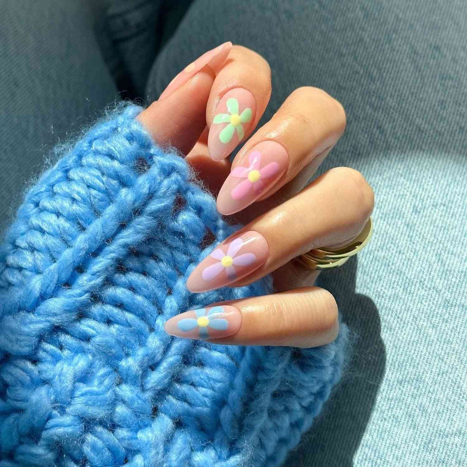 Almond-shaped nail painted with a neutral milklike base topped off with a single pastel daisy per nail