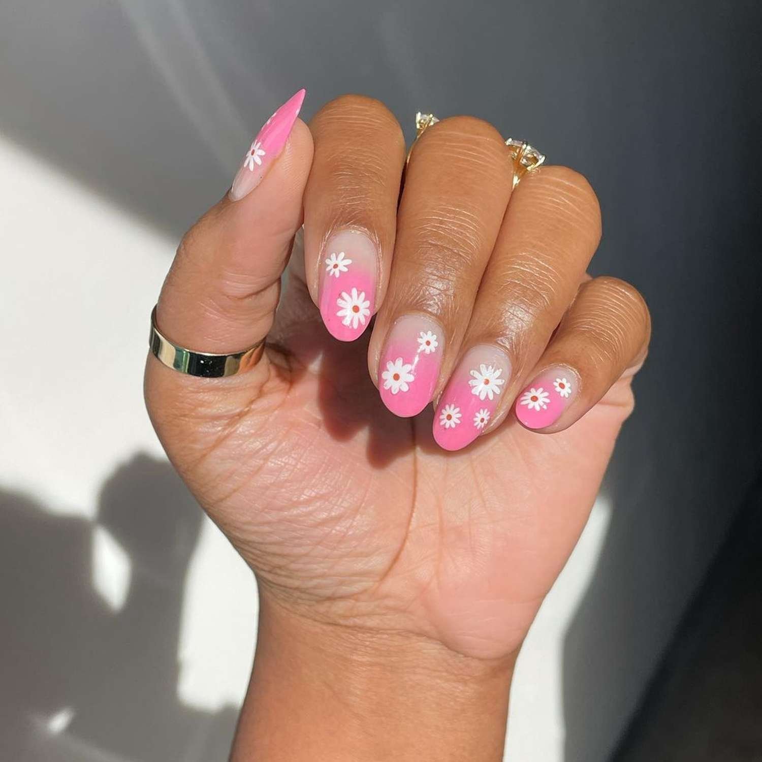 Hand showcasing angstrom unit pink ombre manicure with white daisies on top