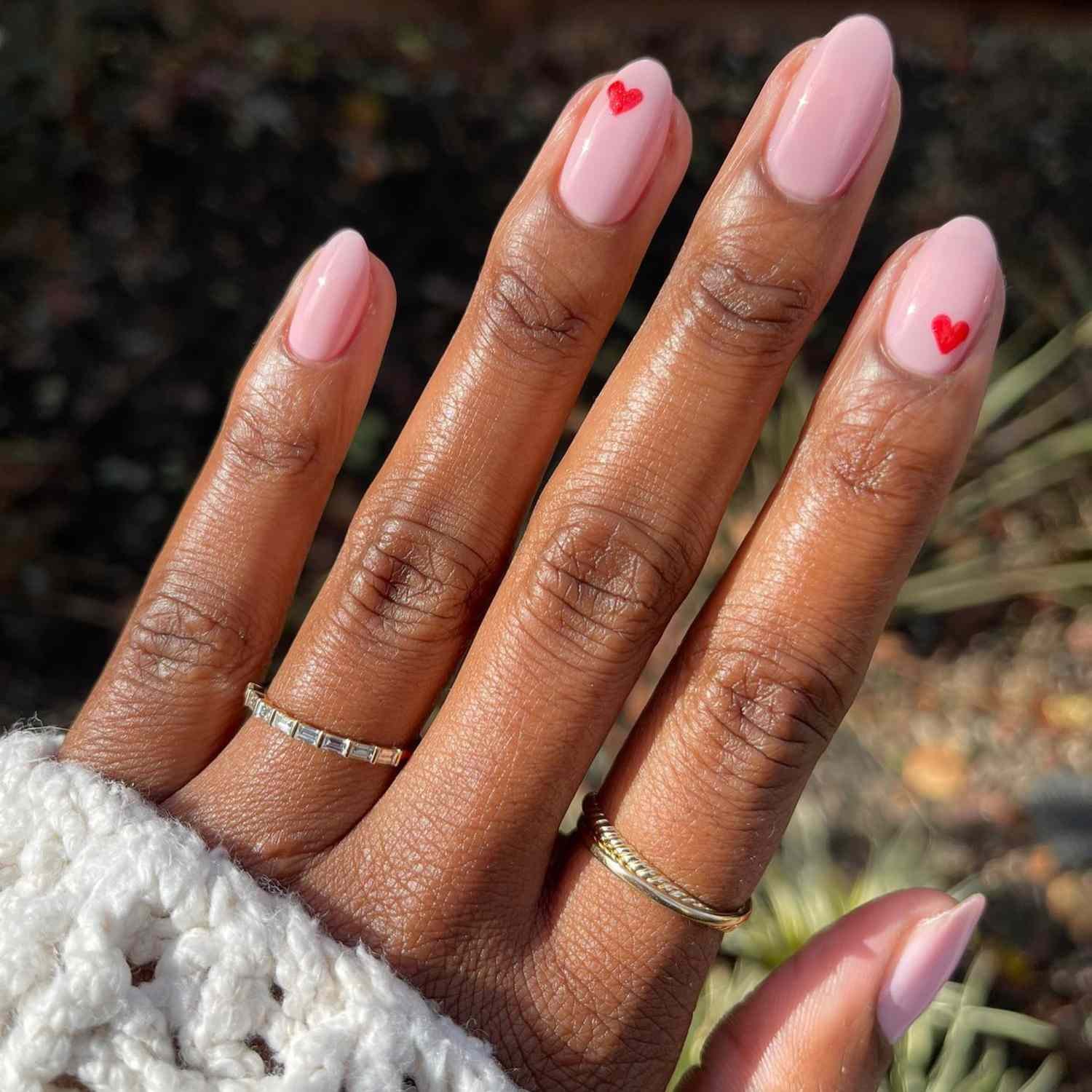 close up of nail with light pink manicure with redness hand paint hearts