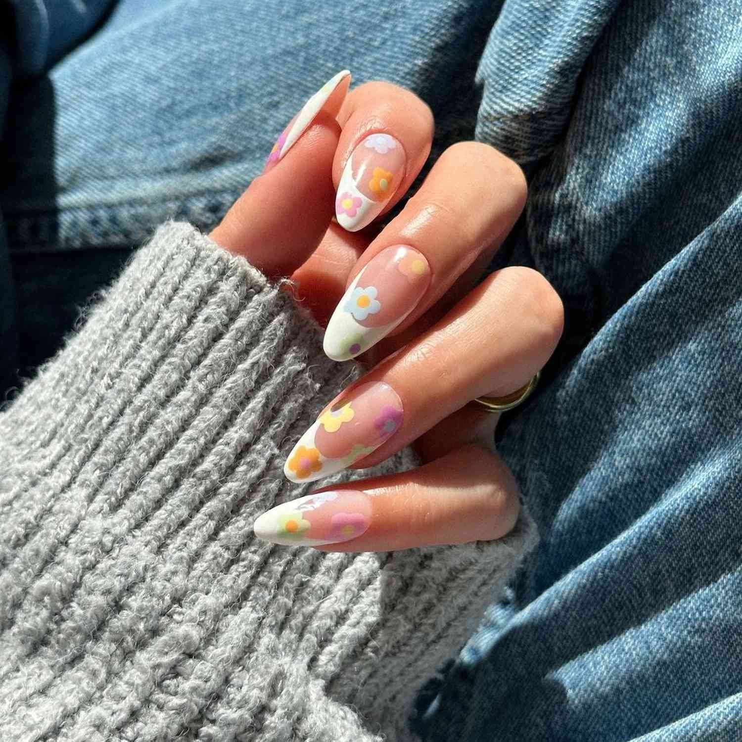 Hand with nails paint inch a white French tip design with colourful pastel flower on top