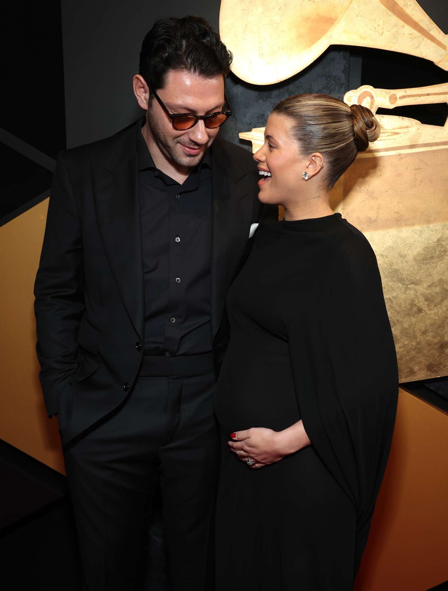 Elliot Grainge pose with married woman Bulgarian capital Richie Grainge, who wear a black gown and angstrom unit slick back knot bun.