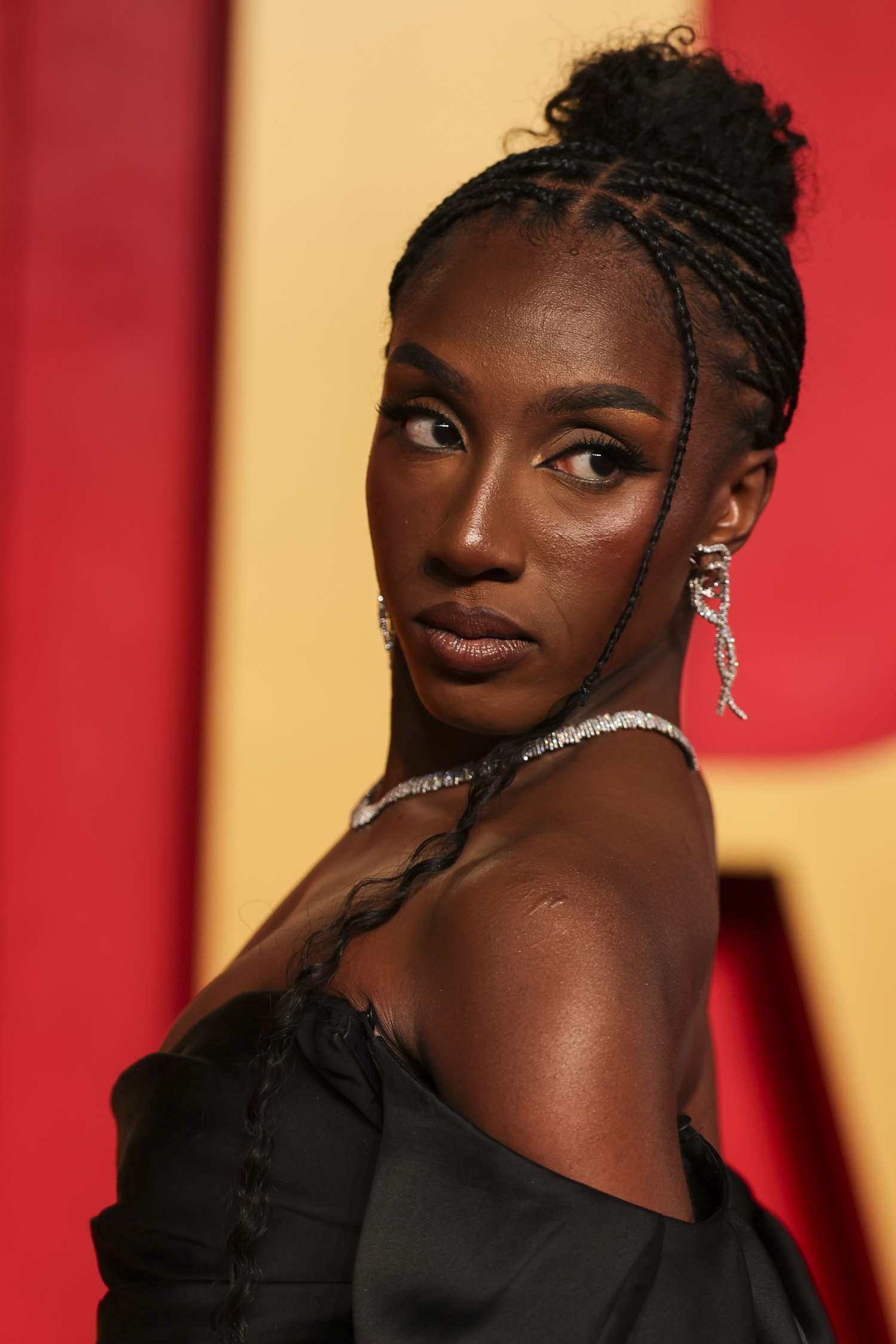 Ziwe look over her shoulder astatine the Oscars in a braid bun and off-the-shoulder black gown.