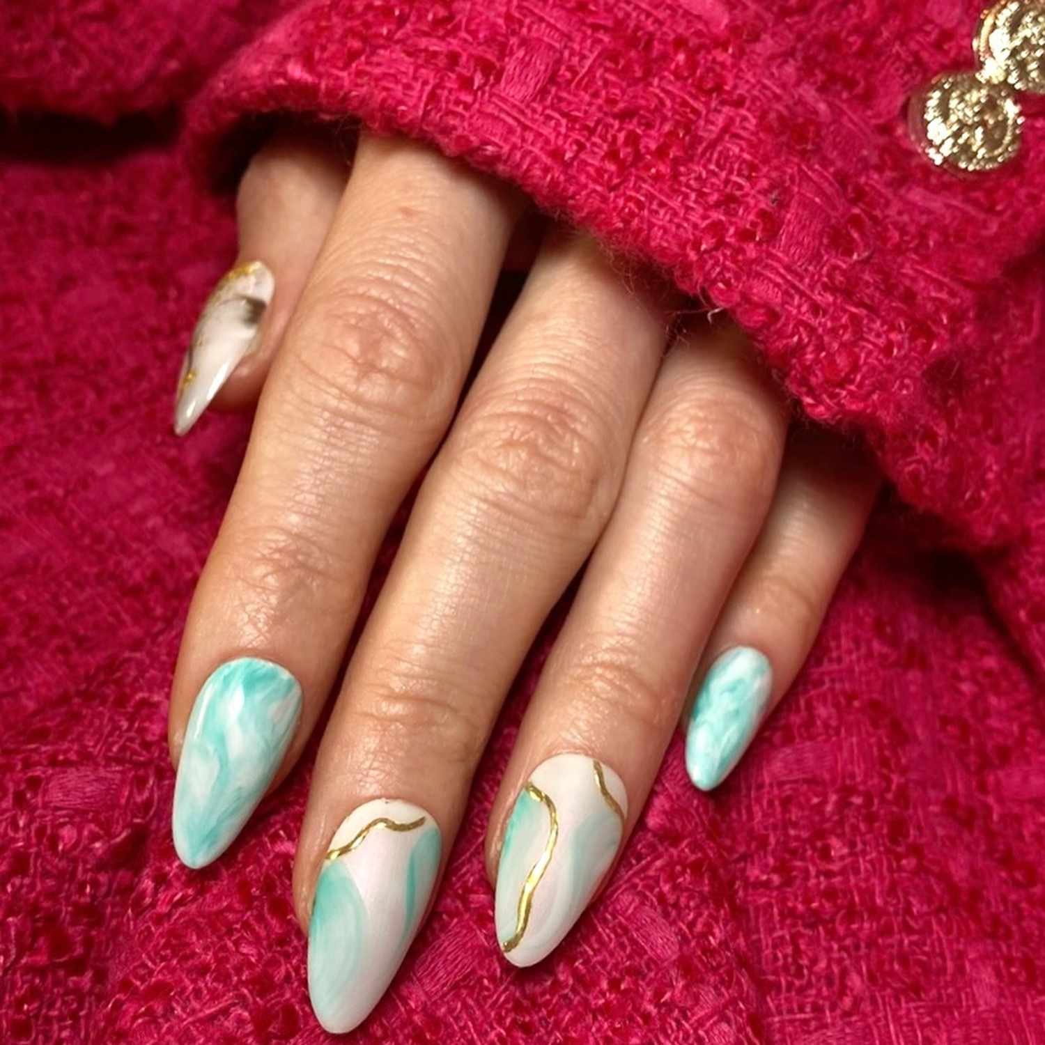 Mint marble manicure with gold accents, on a reddish-pink knit background