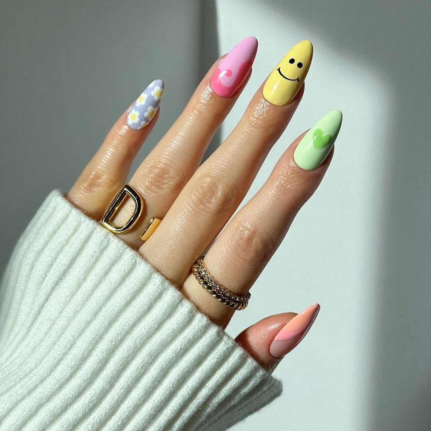 Almond-shaped nail showcasing A pastel mismatch manicure with flowers, a heart, yin-yang, and smiley face