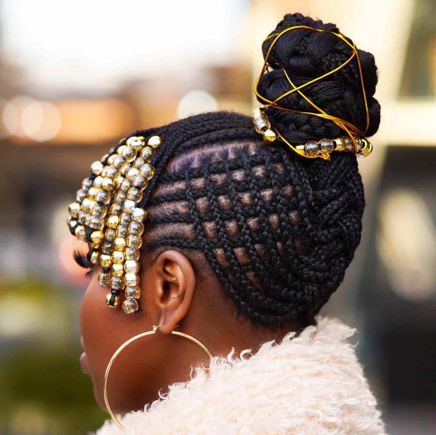 A person with an intricate braided updo with gold accessories and gold beaded bangs